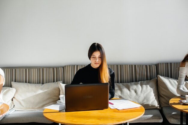 Ein junges schönes Mädchen sitzt in einem Café, arbeitet am Computer und kommuniziert in sozialen Netzwerken.