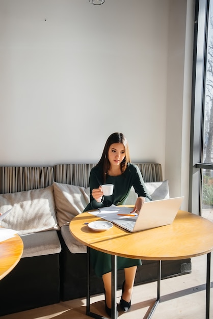 Ein junges schönes Mädchen sitzt in einem Café, arbeitet an einem Computer und kommuniziert in sozialen Netzwerken.