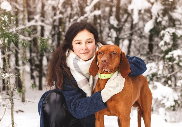 Ein junges schönes Mädchen umarmt im Winter einen rothaarigen Hund im Wald. Menschliche Freundschaft mit Tieren