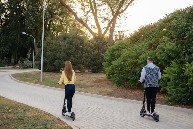 Ein junges schönes Paar fährt an einem warmen Herbsttag mit Elektrorollern im Park