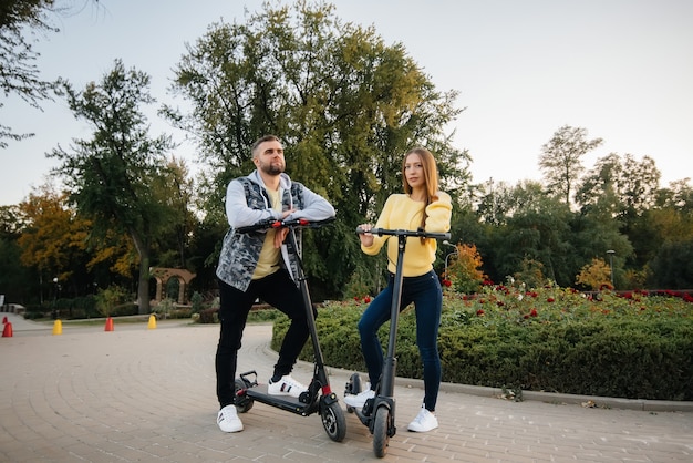 Ein junges schönes Paar fährt an einem warmen Herbsttag mit Elektrorollern im Park