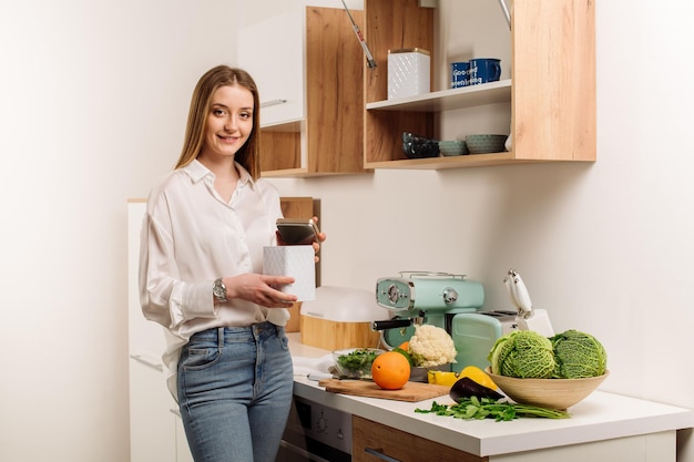 Ein junges schönes vegetarisches Mädchen oder Bloggerin bereitet zu Hause im Küchenblog über gesunde Ernährung ein Frühstück mit Obst, Gemüse und Gemüse zu