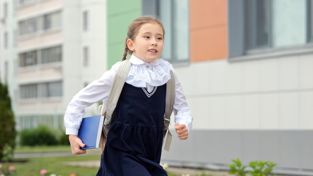 Ein junges Schulmädchen mit Buch rennt zur Grundschule