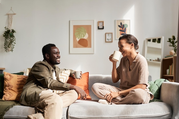 Ein junges schwarzes Paar sitzt in einem gemütlichen Zuhause auf der Couch und unterhält sich