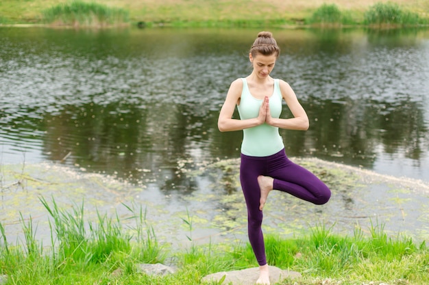 Ein junges Sportmädchen praktiziert Yoga auf einer grünen Wiese am Fluss