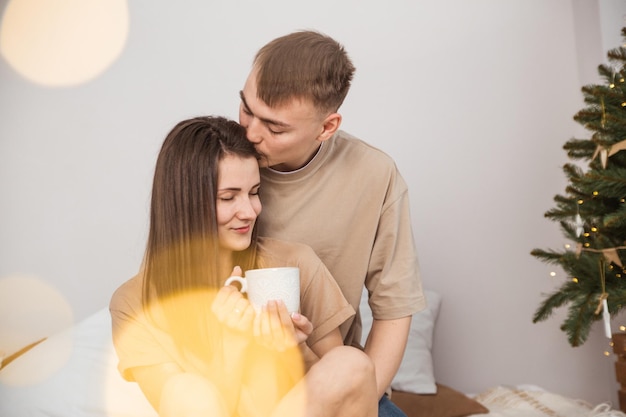 ein junges verliebtes paar sitzt auf dem bett, umarmt sich lächelnd und trinkt morgens kaffee