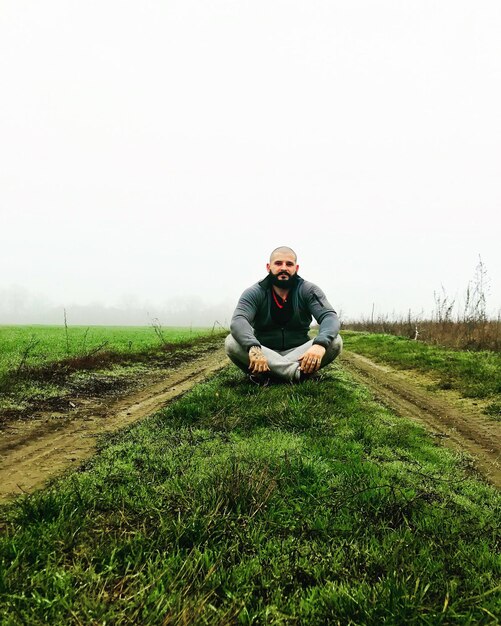 Ein kahlköpfiger Mann sitzt auf dem Feld vor klarem Himmel