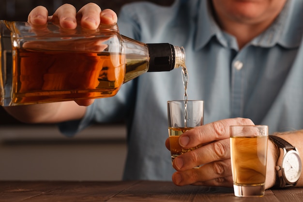 Ein kaukasischer Mann Hände schließen nah, Alkohol in ein Glas gießend