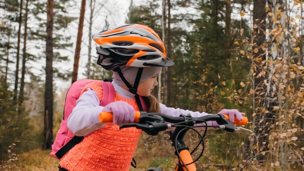 Ein kaukasisches Kind geht mit dem Fahrrad im Herbstpark. Kleines Mädchen, das in Fores schwarz-orange radfährt