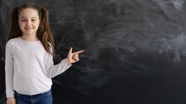 Ein kaukasisches Mädchen, ein Schulmädchen, steht vor dem Hintergrund einer leeren Kreidetafel, der Zeigefinger zeigt auf einen leeren Platz für Text c