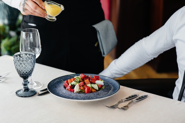 Ein Kellner gießt Sauce über einen frischen Salat aus Gemüse und Thunfisch in Nahaufnahme. Gesundes Essen.