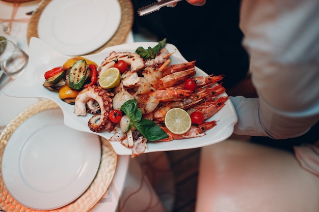 Ein Kellner in einem Restaurant hält Meeresfrüchtegerichte und serviert einen Tisch Catering Konzept Gesundes Essen Oktopus und Krabben Schalentiere.