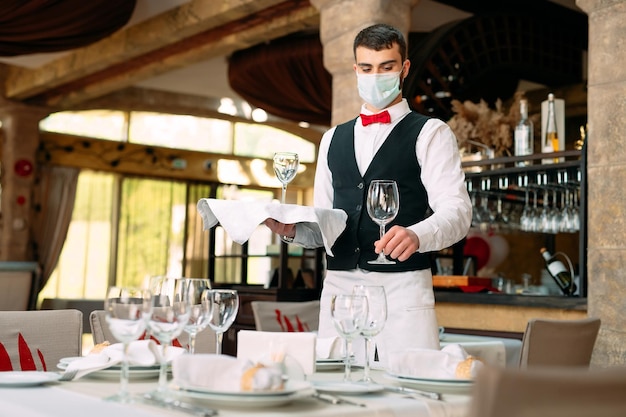 Ein Kellner in einer medizinischen Schutzmaske bedient den Tisch im Restaurant.