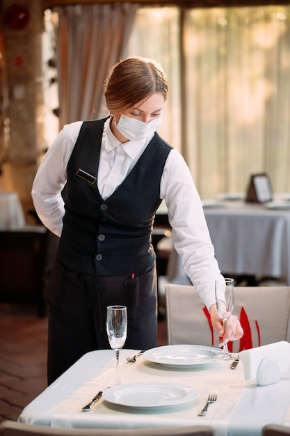 Ein Kellner in einer medizinischen Schutzmaske serviert den Tisch im Restaurant.