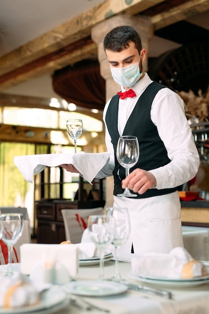 Ein Kellner in einer medizinischen Schutzmaske serviert den Tisch im Restaurant.