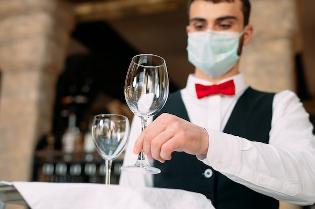 Ein Kellner mit einer medizinischen Schutzmaske serviert den Tisch im Restaurant