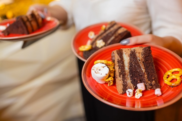 Ein Kellner serviert zwei Stück Kuchen auf Tellern. Mit einer Hand hält er zwei Teller.