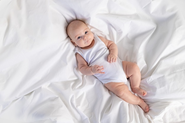 Ein Kind auf einem weißen Bett am Morgen. Textilien und Bettwäsche für Kinder. Ein Neugeborenes ist aufgewacht oder geht ins Bett