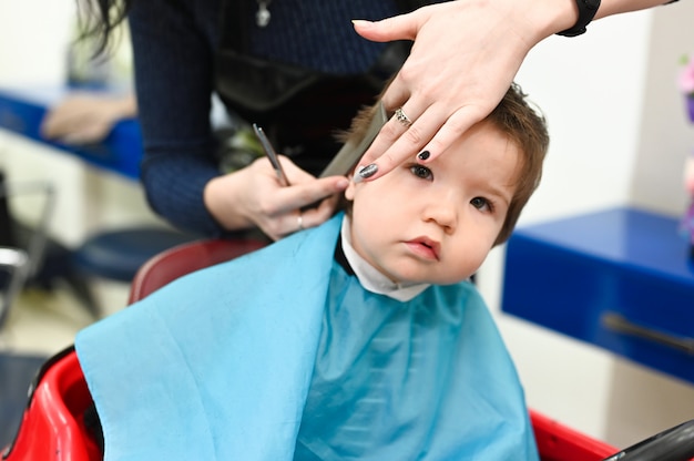 Ein Kind beim Friseur. Der erste Haarschnitt des Kindes beim Friseur. Baby Haarschnitt Kleinkind.