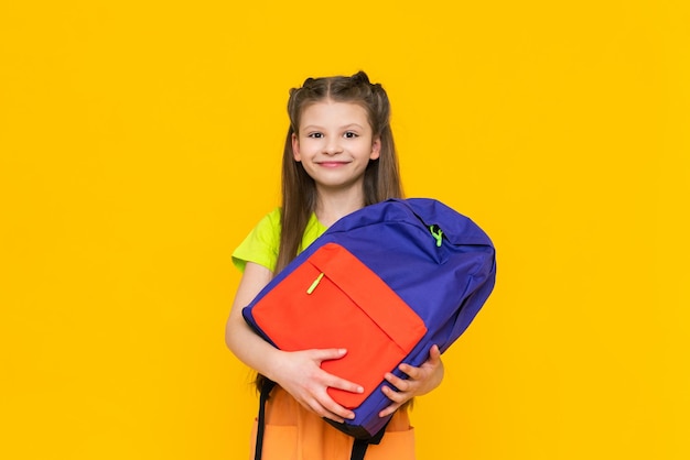 Ein Kind hält einen Schulrucksack Ein schönes kleines Mädchen bereitet sich auf das Studium vor Isolierter gelber Hintergrund