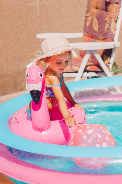 Ein Kind in einem aufblasbaren Pool badet im Garten in einem Hut und einem Badeanzug