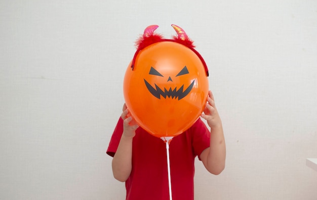 Ein kind in einem kostüm hält gruselige luftballons für halloween auf einem weißen hintergrund.