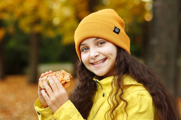 Ein Kind in gelber Kleidung mit einem Hamburger in der Hand schaut in die Kamera und lächelt im Park