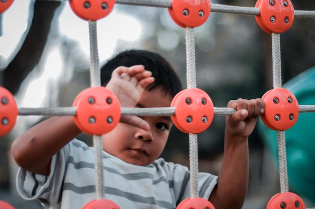 Ein Kind klettert an einem heißen Sommertag in einem Park auf einem Spielplatz auf ein alpines Gitter. Kinderspielplatz in einem öffentlichen Park Unterhaltung und Erholung für Kinder