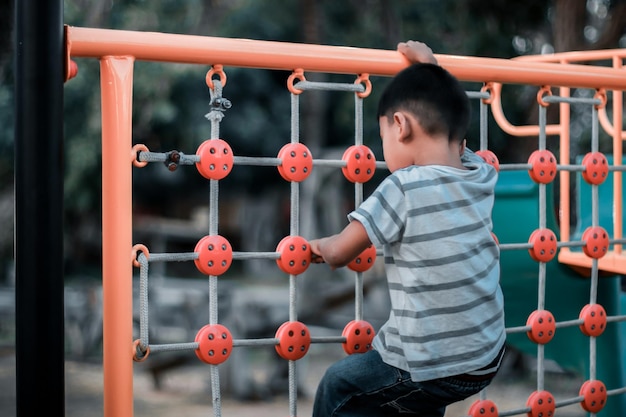 Ein Kind klettert an einem heißen Sommertag in einem Park auf einem Spielplatz auf ein alpines Gitter. Kinderspielplatz in einem öffentlichen Park Unterhaltung und Erholung für Kinder