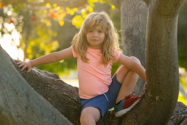 Foto ein kind klettert auf einen baum, ein glücklicher junge spielt im sommergarten, ein kind auf einem baum mit einem großen zweig.