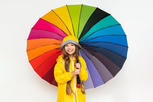 Ein Kind mit einem bunten Regenschirm in einem gelben Regenmantel und einem Panamahut auf einem weißen, isolierten Hintergrund
