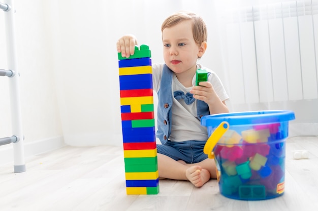 Ein Kind mit einem Konstrukteur zu Hause, ein süßer Junge spielt oder sammelt einen farbigen Konstrukteur