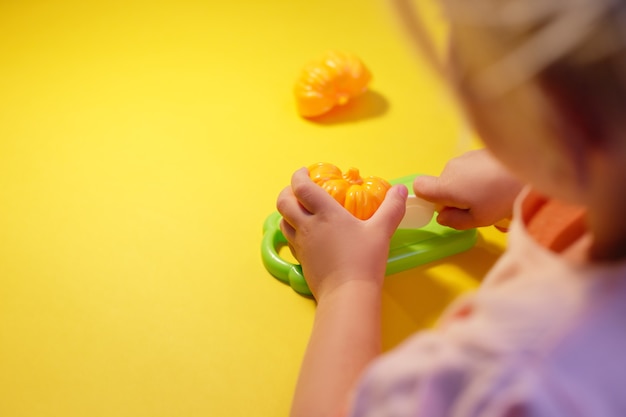 Ein Kind schneidet mit einem Spielzeugmesser einen Spielzeugpaprika auf gelbem Grund