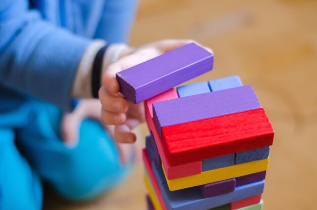 Foto ein kind spielt ein spiel mit farbigen holzklötzen, jenga-nahaufnahme, selektiver fokus