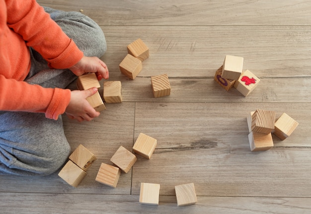 Foto ein kind spielt zu hause auf dem boden mit holzwürfeln. der blick von oben.