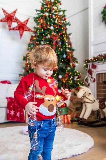 Ein Kind tanzt in der Nähe eines Weihnachtsbaums mit einer Girlande. Selektiver Fokus