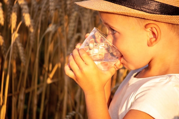 Ein Kind trinkt Wasser auf dem Hintergrund des Feldes