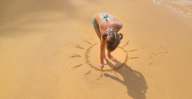 Ein Kind zeichnet eine Sonne am Strand.