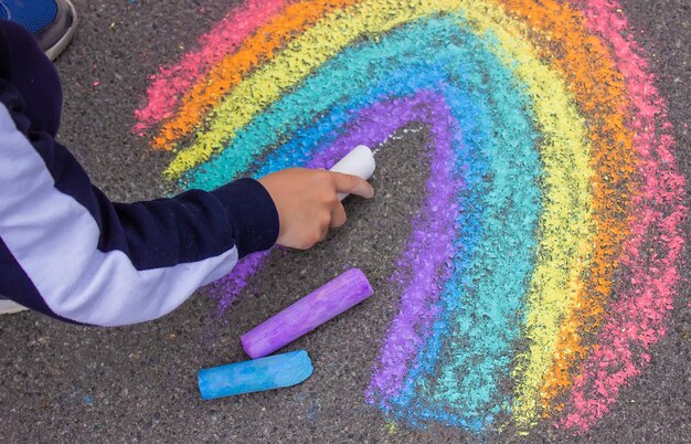 Ein Kind zeichnet einen Regenbogen auf den Asphalt Selektiver Fokus