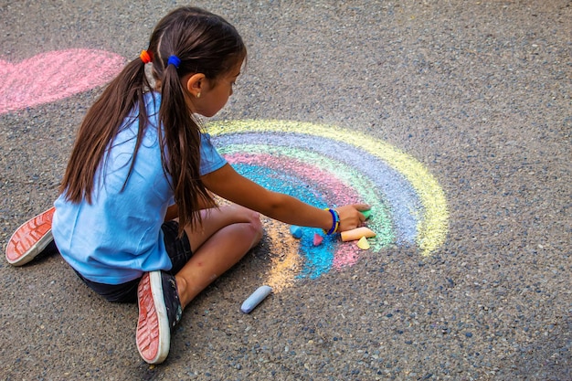 Ein Kind zeichnet einen Regenbogen auf den Asphalt Selektiver Fokus