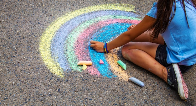 Ein Kind zeichnet einen Regenbogen auf den Asphalt Selektiver Fokus