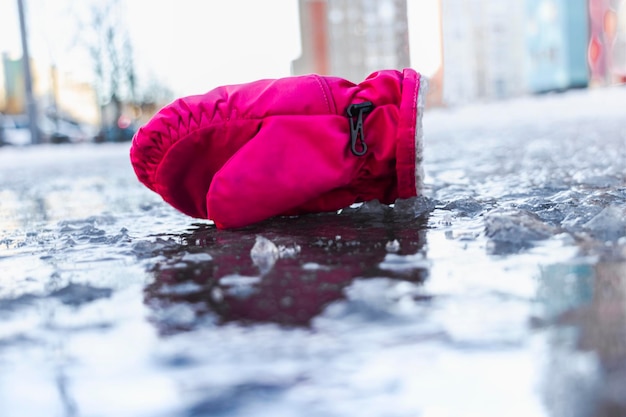 Ein Kinderhandschuh auf einer rutschigen Straße aus geschmolzenem Eis Frühlingstauwetter und Eis Winterstraße in der Stadt Verletzungen und Folgen nach einem Sturz auf einer vereisten Straße