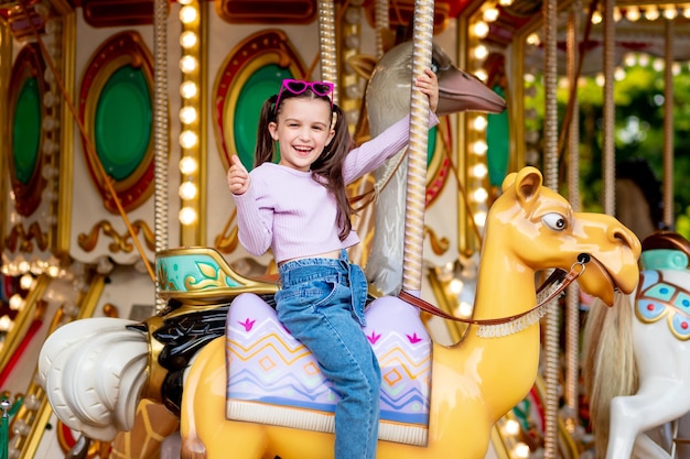 Ein Kindermädchen in einem Vergnügungspark fährt auf einem Karussell und lächelt vor Glück und zeigt der Klasse das Konzept der Wochenenden und Schulferien