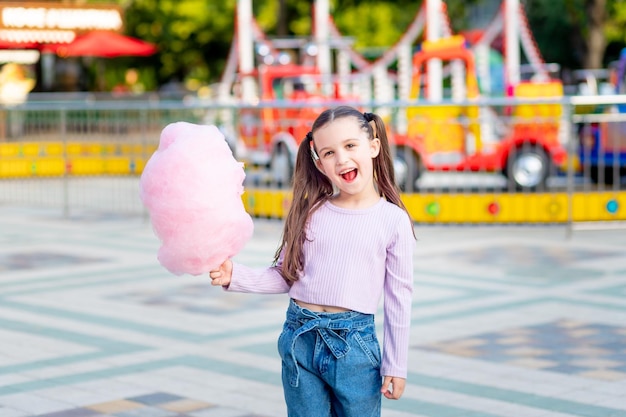 Ein Kindermädchen in einem Vergnügungspark isst im Sommer Zuckerwatte in der Nähe der Karussells das Konzept der Sommerferien und Schulferien