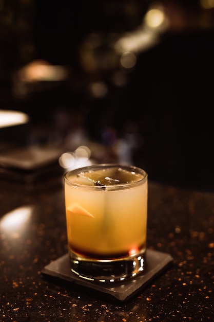 Ein klassischer saurer Cocktail on the rocks in einem altmodischen Glas mit Orangenschale an der Bar