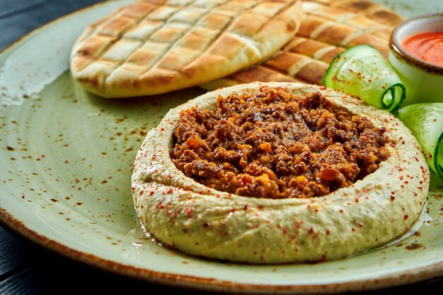 Ein klassisches orientalisches Gericht - Kichererbsen-Hummus mit Olivenöl und Hackfleisch, serviert mit gebackenem Pita in einem Teller auf einer dunklen Holzoberfläche. Vegetarisches Essen. Diät