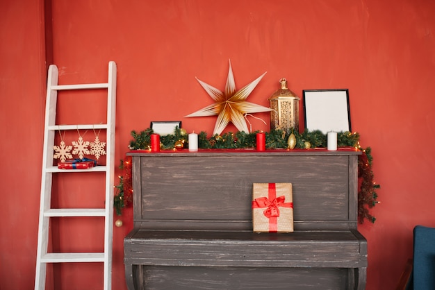 Ein Klavier mit Weihnachtsschmuck und eine weiße Treppe im Haus an einer roten Wand