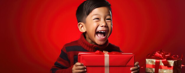 Ein kleiner afrikanischer Junge öffnet ein Geschenk und lacht auf rotem Hintergrund.