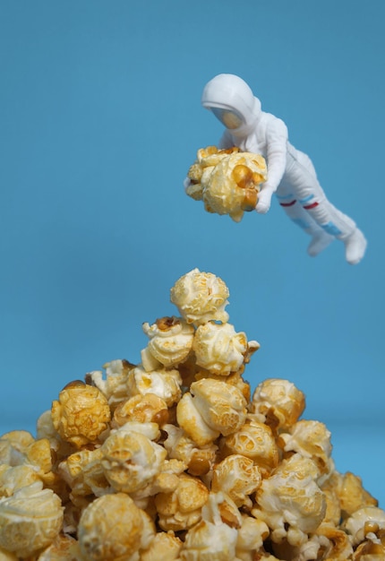 Foto ein kleiner astronaut trägt ein riesiges popcorn aus dem haufen mit blauem hintergrund