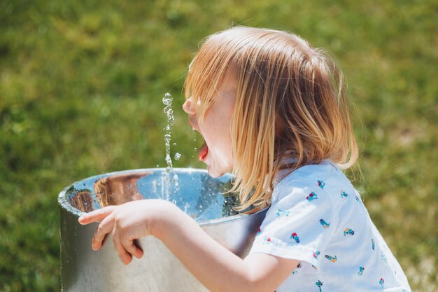 Foto ein kleiner blonder junge trinkt an einem heißen sommertag im freien aus einem trinkbrunnen in einem stadtpark